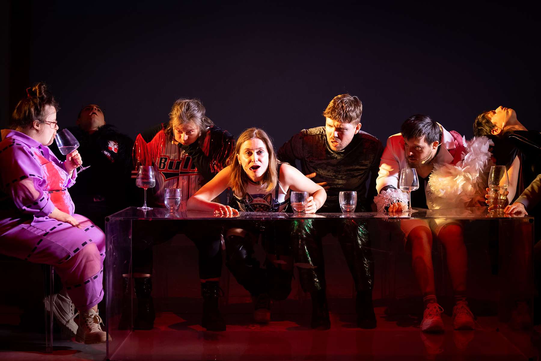 W kostiumach zwierzęcych aktorzy Teresa Foks, Piotr Sakowski, Aleksandra Skotarek, Helena Urbańska, Daniel Kotowski, Daniel Krajewski i Ania Nowak siedzą przy długim stole z przezroczystej pleksi - na stole stoją zdobne kieliszki