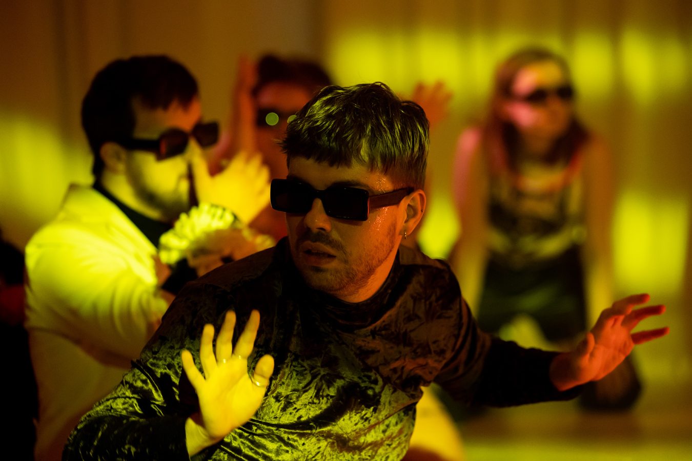 Aktorzy, w plamie złoto-zielonego światła, stoją w okularach przeciwsłonecznych